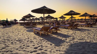 Boş plajda şezlong ve ahşap harika gün batımı tutuyor