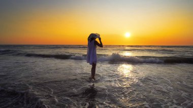 şapkalı günbatımı arka plan üzerinde beyaz elbiseli kadın