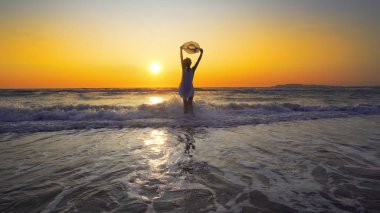 Beyaz elbiseli kadınla şapka duran dalgalar günbatımı arka plan üzerinde