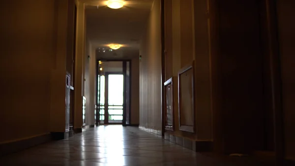 Low angle walk move through long, empty dark building corridor, cinematic steadicam shot