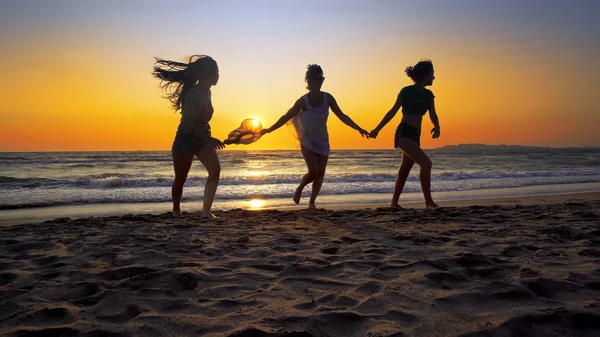 夕日を背景にビーチで海の波で楽しんで幸せな女の子のグループ — ストック写真