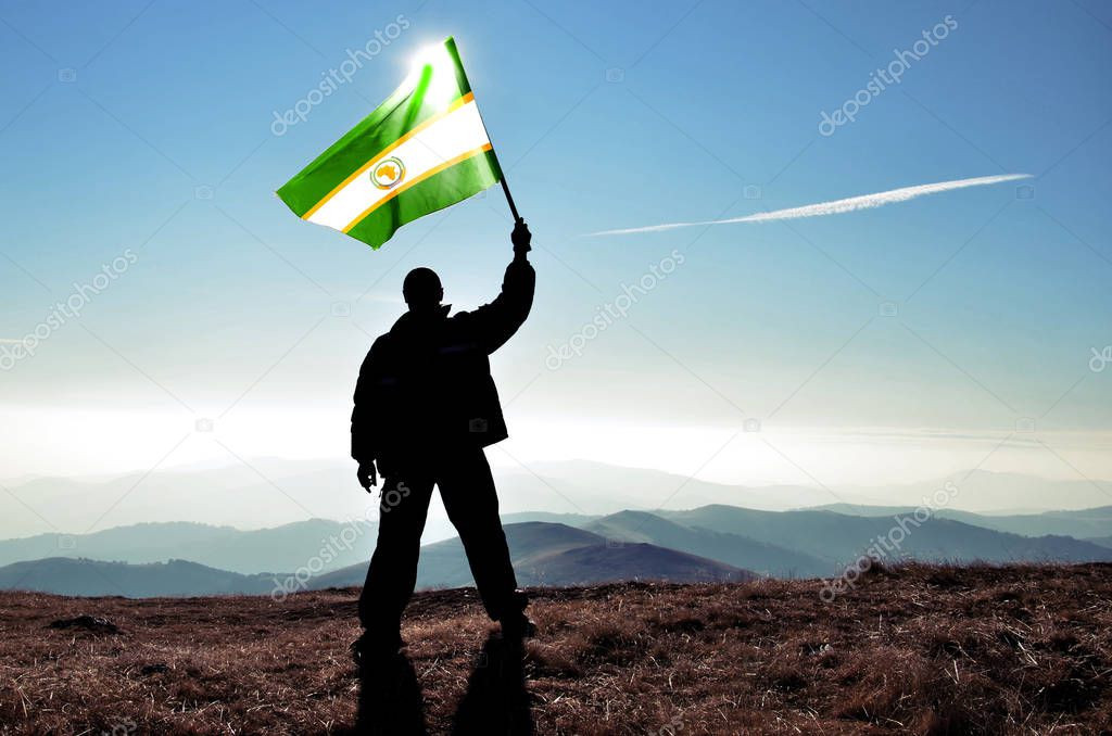 silhouette of man holding waving Organization of African Unity flag on top of mountain peak