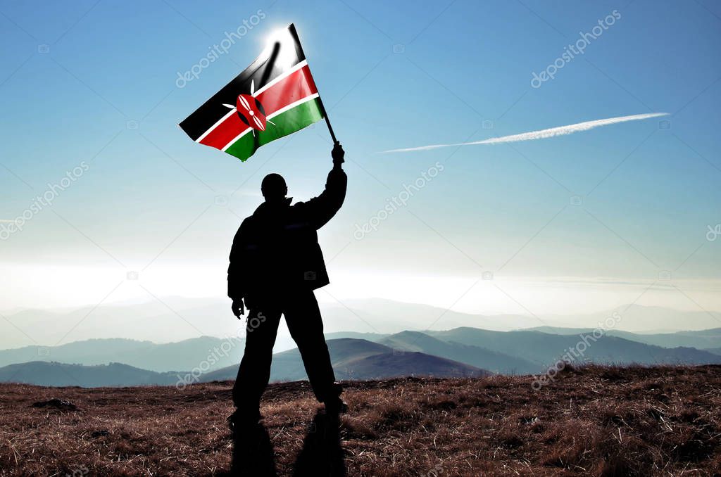 silhouette of man holding waving Kenya flag on top of mountain peak