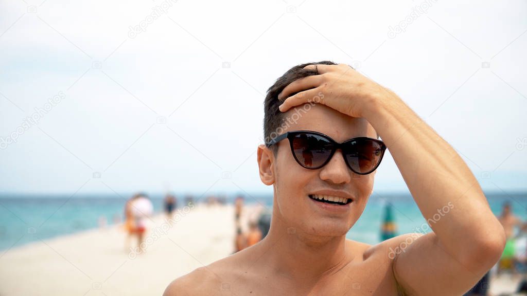 portrait of young man in sunglasses on beach at daytime