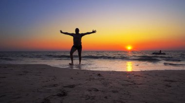 Tanımlanamayan siluet, okyanustan gün batımı suyunda elleri açık, sabit sinematik bir çekimle çıkıyor.