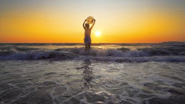 gün batımı arka plan üzerinde beyaz elbise holding şapkalı kadın