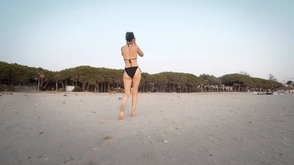 Rear view of woman in bikini walking on empty beach