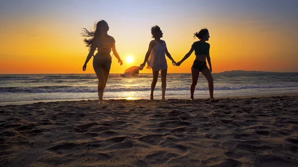 夕日を背景にビーチで海の波で楽しんで幸せな女の子のグループ — ストック写真