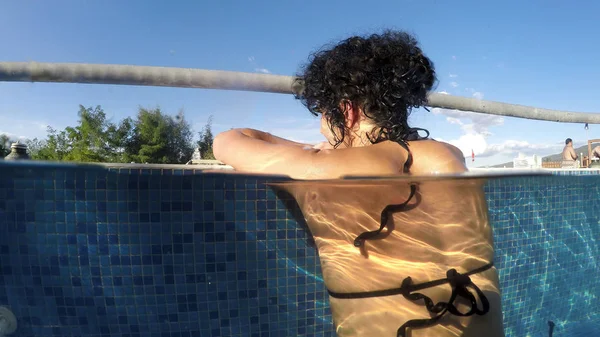 rear view of woman relaxing in outdoor spa swimming pool at daytime