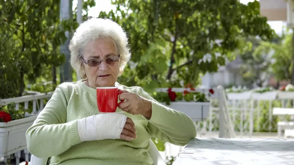 Elderly Old Woman Injured Hand Sitting Drinking Coffee Outdoor — Stock Photo, Image