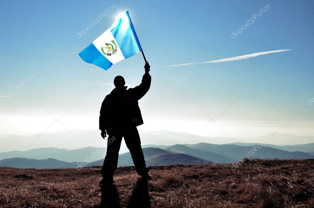 silhouette of man holding waving Guatemala flag on top of mountain peak