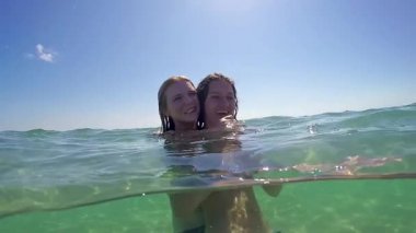 İki genç kız aşk kucaklama içinde ve deniz turkuaz suyu gülümseme, gopro kubbe yarım sualtı görünümü, ağır çekim