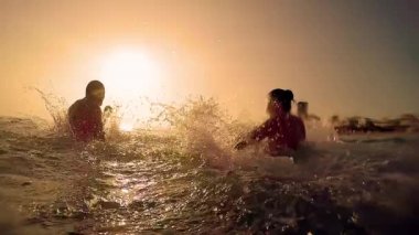 Mutlu aile sıçramasına, oynarken su sahilde sunset Bulvarında püskürtme grubudur. Yaz günbatımı üzerinde. Plaj partisi. Ağır çekim yaz