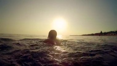Woman playing swimming in the sea at sunset, trekking shot