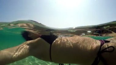 Sakin su yüzeyinde yüzen esmer kıvırcık kadın seksi mayo içinde sualtı