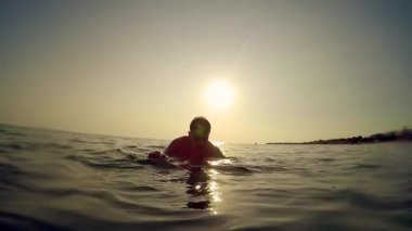 Young man stands on his friend shoulder in sea at sunset, slow motion