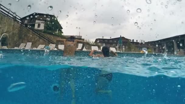 2人の女の子が泳いで雨天にプールを出る ゴプロドーム半分の水中ビュー スローモーション — ストック動画