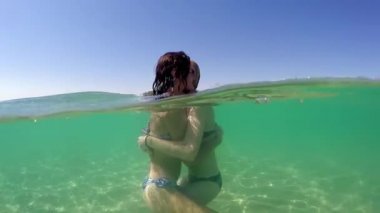 En yakın arkadaşlarım sarılma. İki sevimli kız, veren gençler öpmek ve sarılmak tropikal plaj yaz tatile gopro kubbe yarım sualtı görünümü, ağır çekim