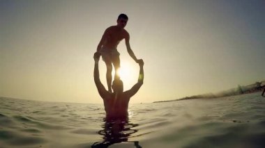 Genç adam parcour backflip deniz günbatımı, ağır çekim, omzundan babası üzerinden atlamak