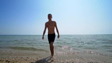Handsome athlete male walk out of water on sea beach, cinematic steadicam shot, SLOW MOTION