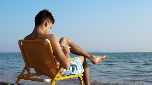 Manlig Tonåring Läsning Stranden — Stockvideo