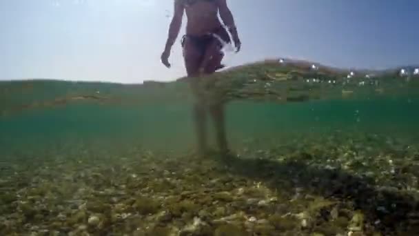 石でビーチの浅い海水を歩くセクシーなファッションモデルの足 ゴプロドームショット — ストック動画