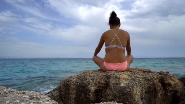 坐在石头上的美丽的妇女在海滩上练习瑜伽冥想 — 图库视频影像