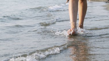 Kadın çıplak ayakla bacaklar dalgalar tarafından sıçrayan deniz kıyısında sinema steadicam vurdu yürüyüş closeup önden görünümü