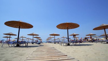 Yaz plaj resort bar lounge alanı ahşap rahat koltuklar ve deniz suyu yanında dizilmiş saman şemsiye