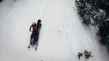 Aerial view of injured snowboarders and snowmobile first aid motor sledge driving on free ride mountain slope among forest pine trees clipart