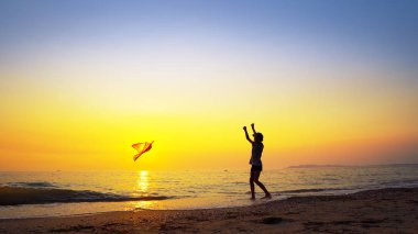 Yaz tatil kavramı. Uçurtmayla boş kumsalda günbatımında çalışan genç çocuk