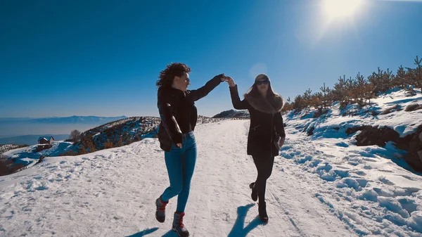 Two happy teen friends running on snow smiling, cinematic steadicam tracking shot