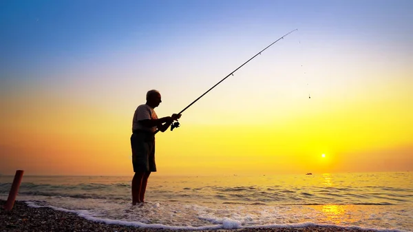 Silhouette of an active fisherman throwing fishing tackles at sea sunset