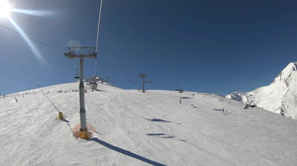 Ski lift with seats going over the mountain with view of people ski and snowboard on slope