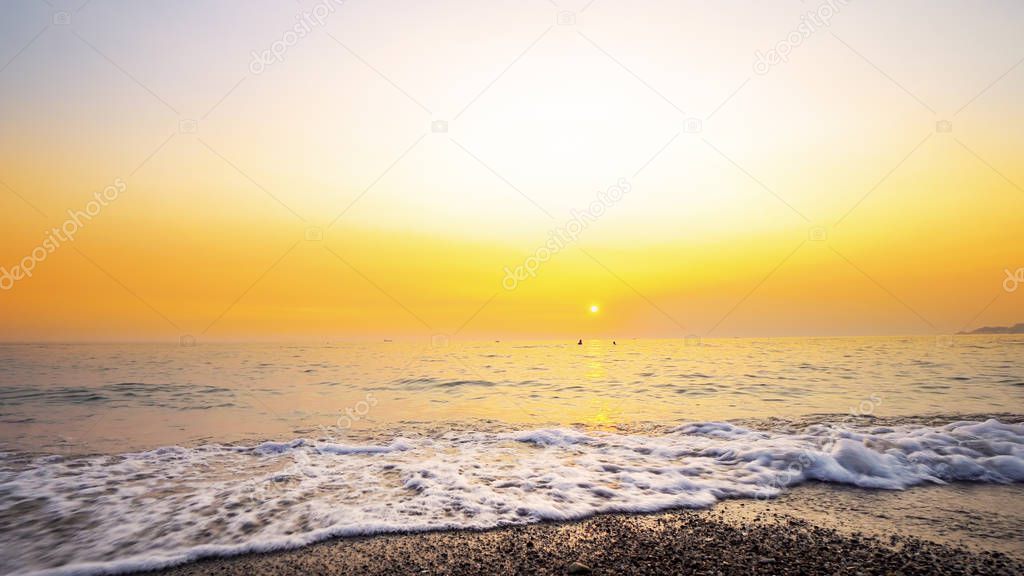 Calm sea waves splash on empty beach at sunset. Wide shot background