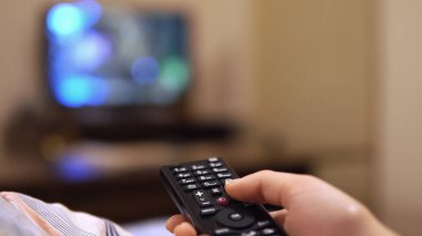 Televizyonun uzaktan kumandasını tutan ve televizyon kanallarını değiştiren bir kadının yakın çekim görüntüsü