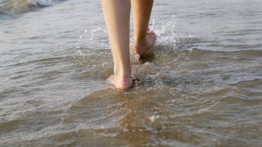 Çıplak ayaklı bir kadının deniz suyu dalgaları üzerinde yürümesi ve sıçraması, sinematik bir çekim.