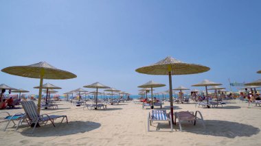 Yaz plaj resort bar lounge alanı ahşap rahat koltuklar ve deniz suyu yanında dizilmiş saman şemsiye