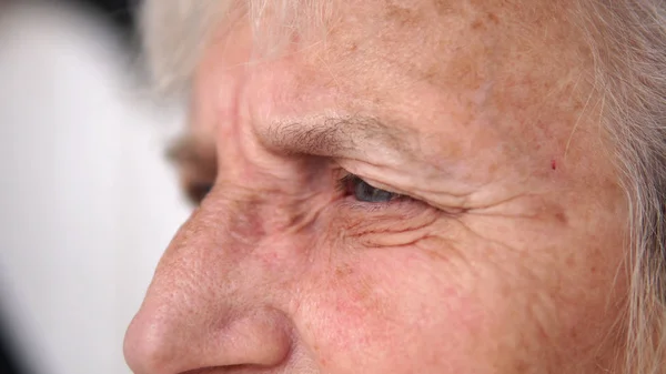 Elderly old woman sad eyes full with tears, closeup with shallow dof