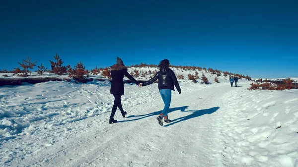 Two happy teen friends running on snow smiling, cinematic steadicam tracking shot