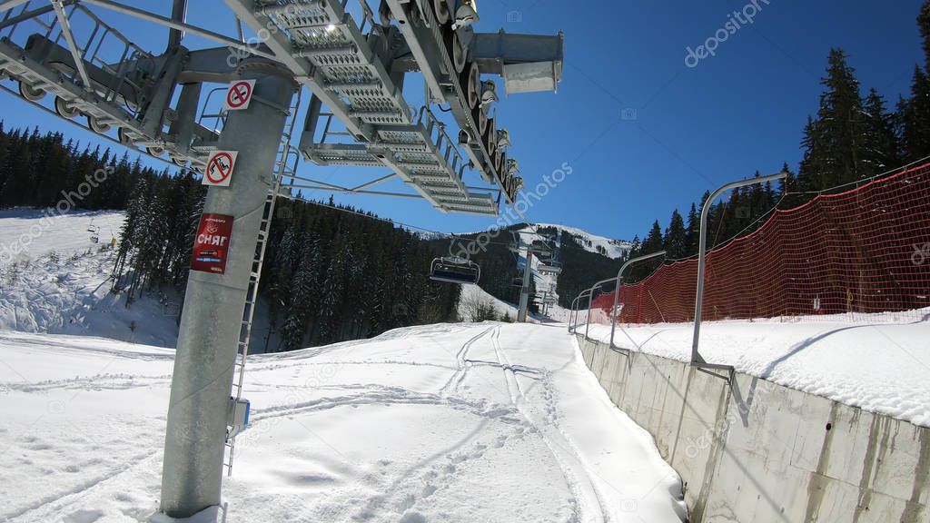 Ski lift with seats going over the mountain with view of people ski and snowboard on slope