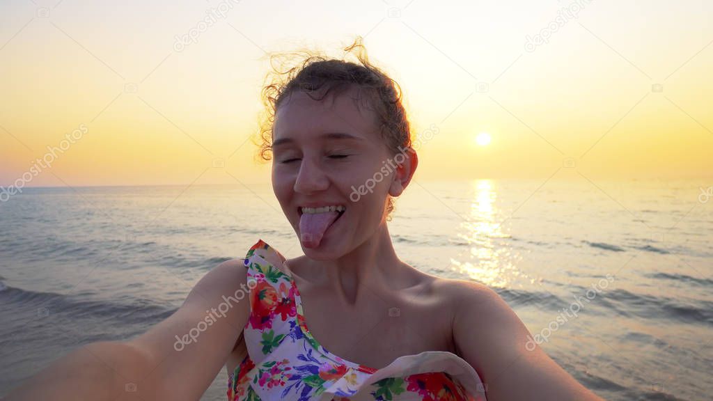 Selfie of young teen holding camera and turning on beach at sunset