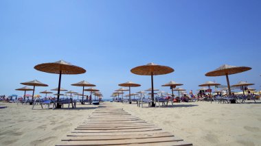 Yaz plaj resort bar lounge alanı ahşap rahat koltuklar ve deniz suyu yanında dizilmiş saman şemsiye