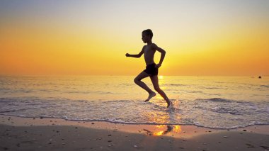 Arka plan gün batımında karşı deniz plaj üzerinde çalışan spor çocuk
