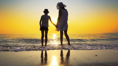 Aile günbatımı ve splash dalgalar deniz sahilde yürümek. Kadın beyaz elbise ve hasır şapka, şapka çocuk vardır