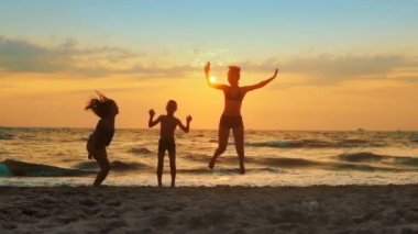 Group of happy children jump at the beach on sunset. Beauty and joyful teenager friends having fun, spraying over summer sunset, SLOW MOTION