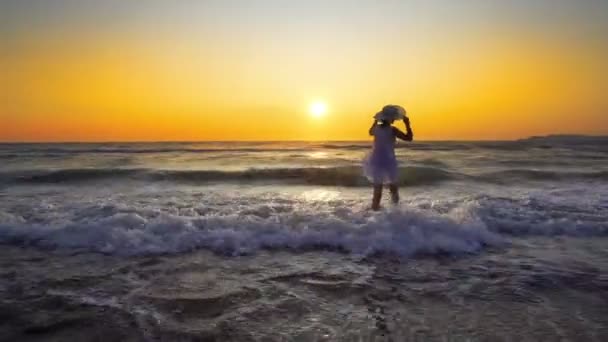 愉快的无忧无虑的女人与帽子和白色礼服享受美丽的日落在海滩上 — 图库视频影像
