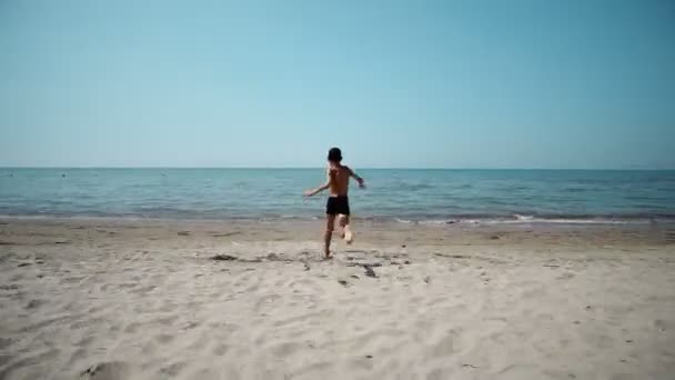 幸せな小さな少年水で実行され ビーチの波で遊ぶ — ストック動画