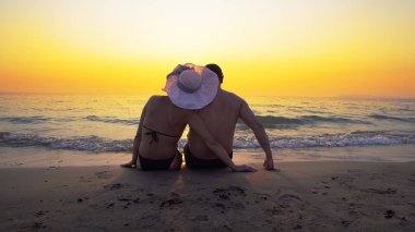 Romantik Çift balayına dokunmadan beach günbatımı ve Satım duyguları üzerinde oturuyor. Yaz dalgalar deniz onların legs splash.
