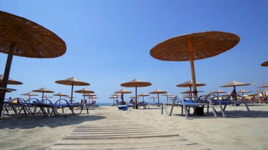 Yaz plaj resort bar lounge alanı ahşap rahat koltuklar ve deniz suyu yanında dizilmiş saman şemsiye